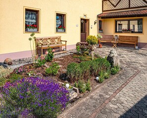 A courtyard with stone paving, wooden benches, and a variety of plants including purple flowers. - The Old Farmhouse (Burgpreppach)