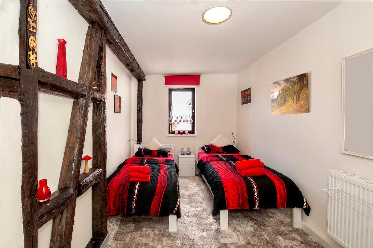 A bedroom with two beds, a window with curtains, a radiator, and a painting on the wall.