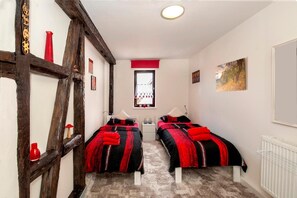 A bedroom with two beds, a window with curtains, a radiator, and a painting on the wall. - The Old Farmhouse (Burgpreppach)