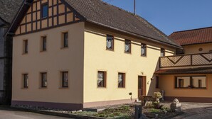 Ein traditionelles Fachwerkhäuschen mit symmetrischer Vorderseite, zahlreichen Fenstern und einem kleinen Gartenbereich mit Topfpflanzen und einer Steinstatue.