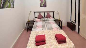 Een slaapkamer met een bed, twee nachtkastjes, een bijzettafeltje, een spiegel en een deur.
