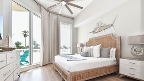 Un dormitorio con una cama grande, ventilador de techo, vista a palmeras y un balcón.