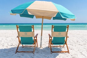 Zwei Strandstühle mit einem Sonnenschirm am Sandstrand.