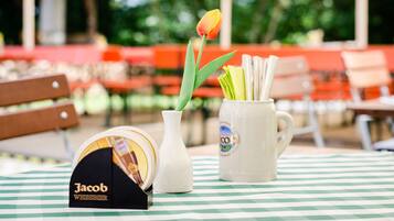 A table with a checkered tablecloth, a white mug with a label, a white vase with a tulip, and a box labeled "Jacob Weissbier".