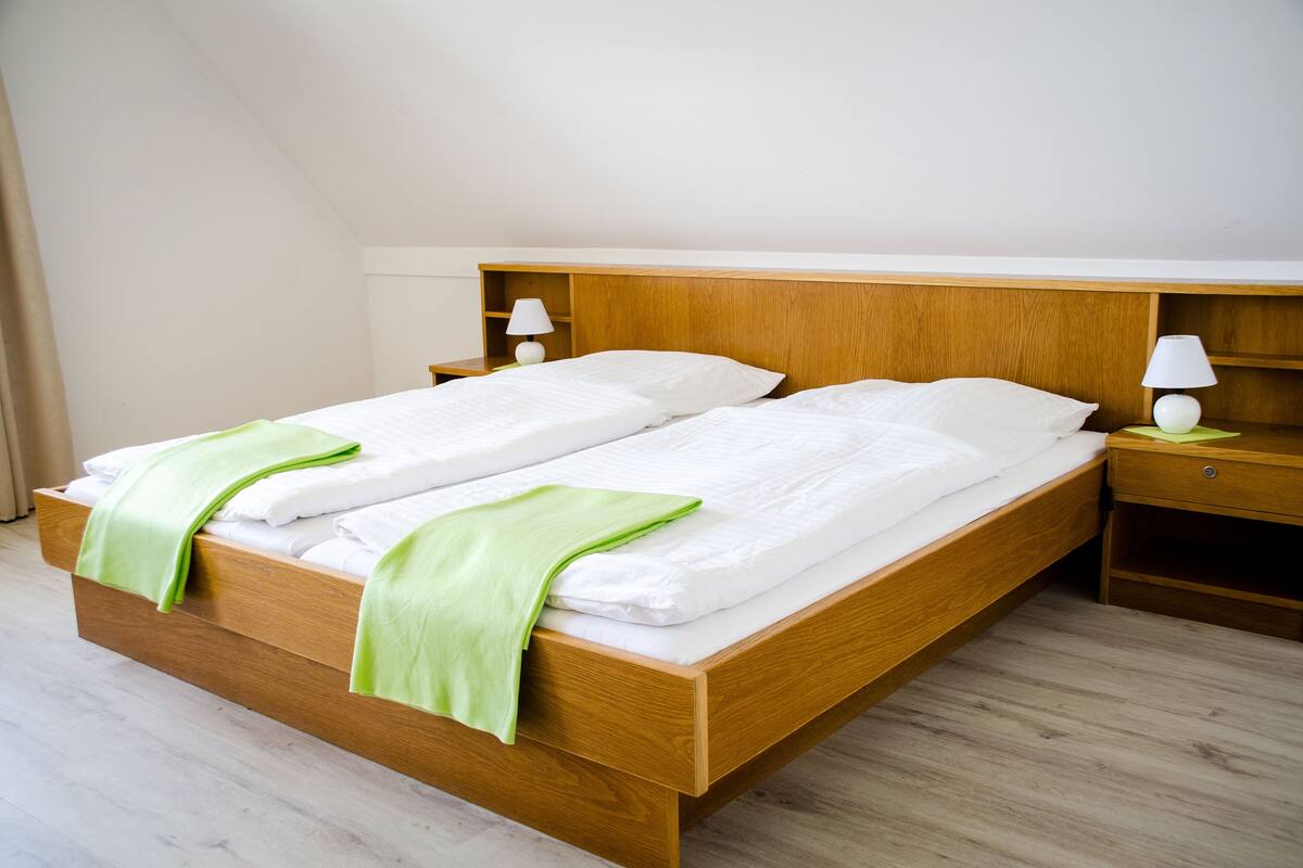 A double bed with a wooden headboard, two bedside tables with lamps, and a green throw blanket.