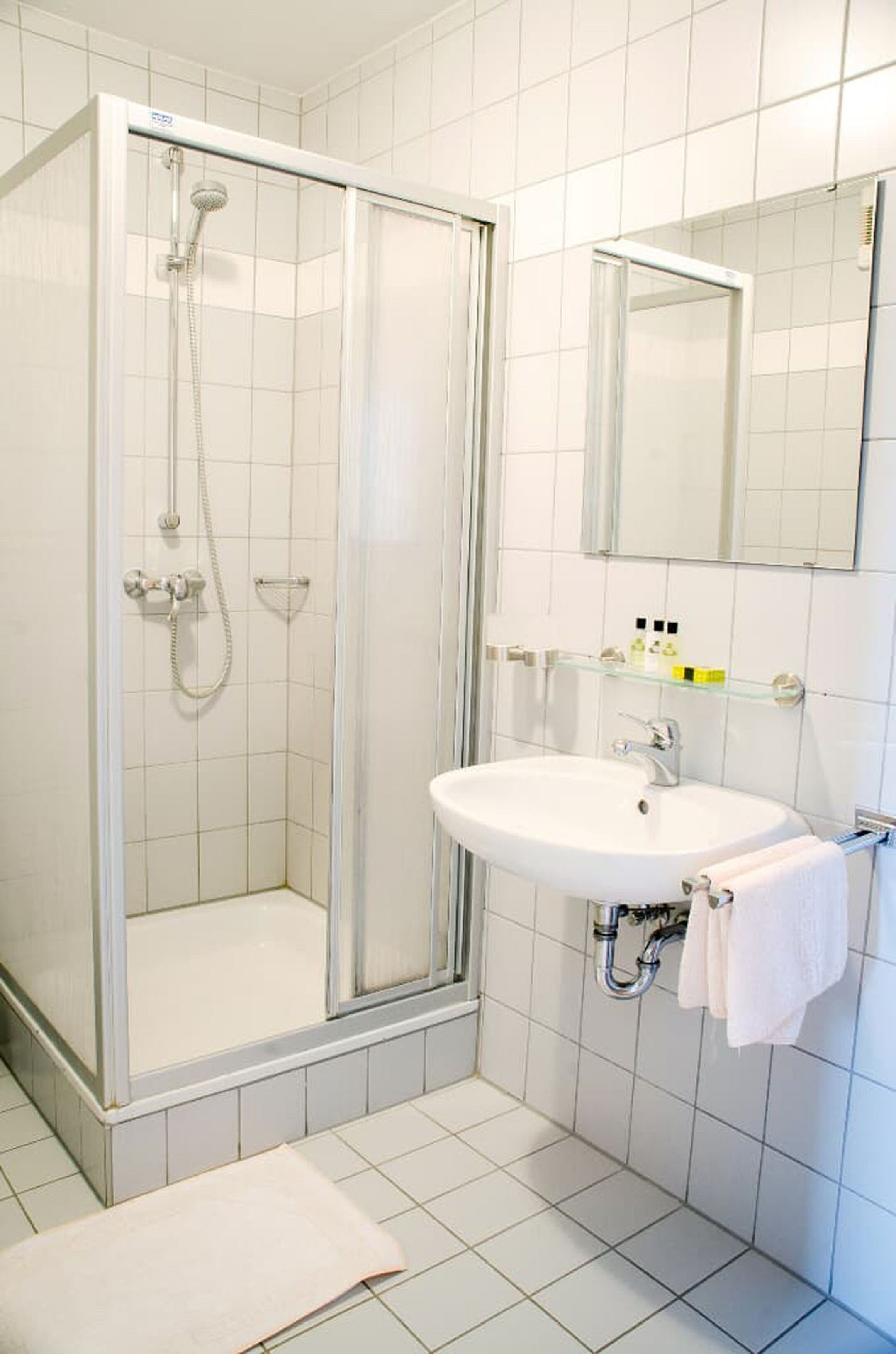 Ein Badezimmer mit einer gläsernen Duschkabine, einem weißen Waschbecken mit Spiegel darüber und einem Handtuchhalter.