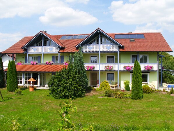 A two-story house with a red-tiled roof, balconies with flower boxes, and a well-maintained lawn. - Landhaus Brummer (Bad Birnbach)
