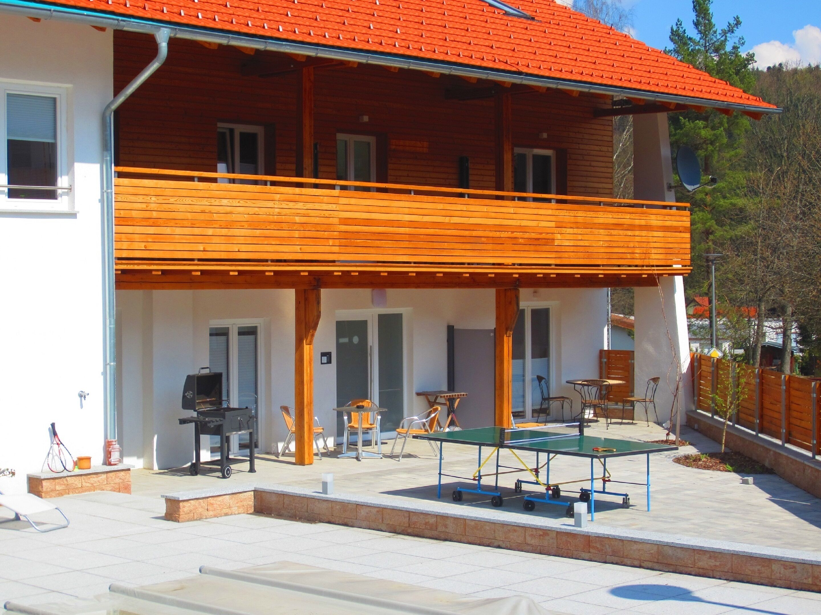 Una casa a due piani in legno con un balcone, posti a sedere all'aperto e un tavolo da ping pong.