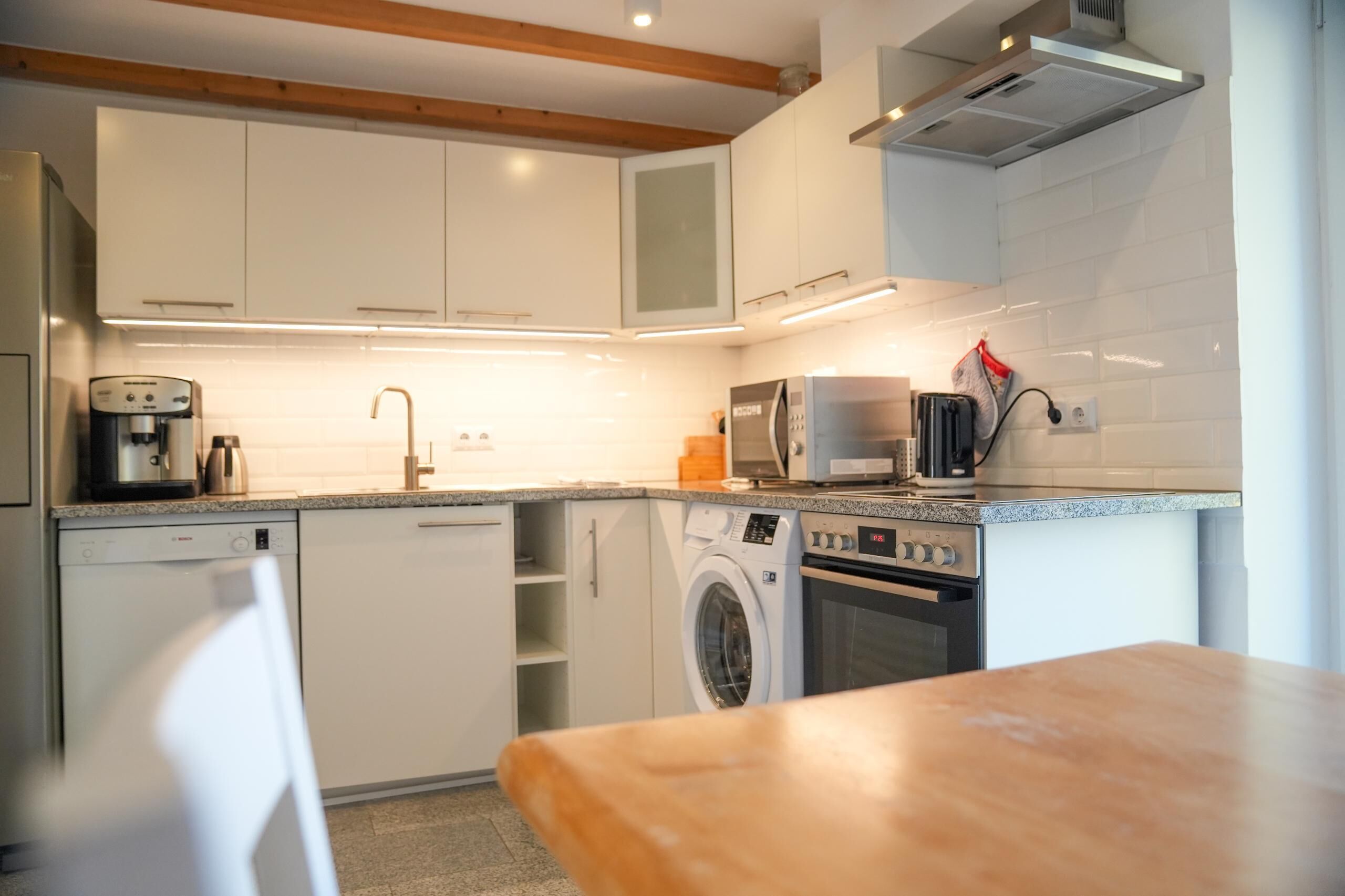 A modern kitchen with white cabinetry, a dishwasher, a washing machine, a microwave, and a coffee maker.