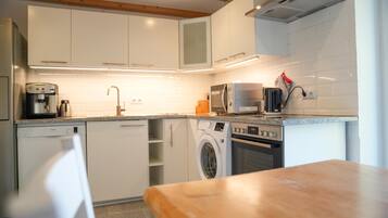 A modern kitchen with white cabinetry, a dishwasher, a washing machine, a microwave, and a coffee maker.