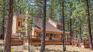 Eine Holzhütte mit einer Holzdiele und großen Fenstern, umgeben von hohen Kiefern.