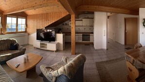 A cozy living room with a sofa, a coffee table, and a TV. There's a kitchen area with cabinets and a dining table. - Ferienwohnungen Martina (Windorf)