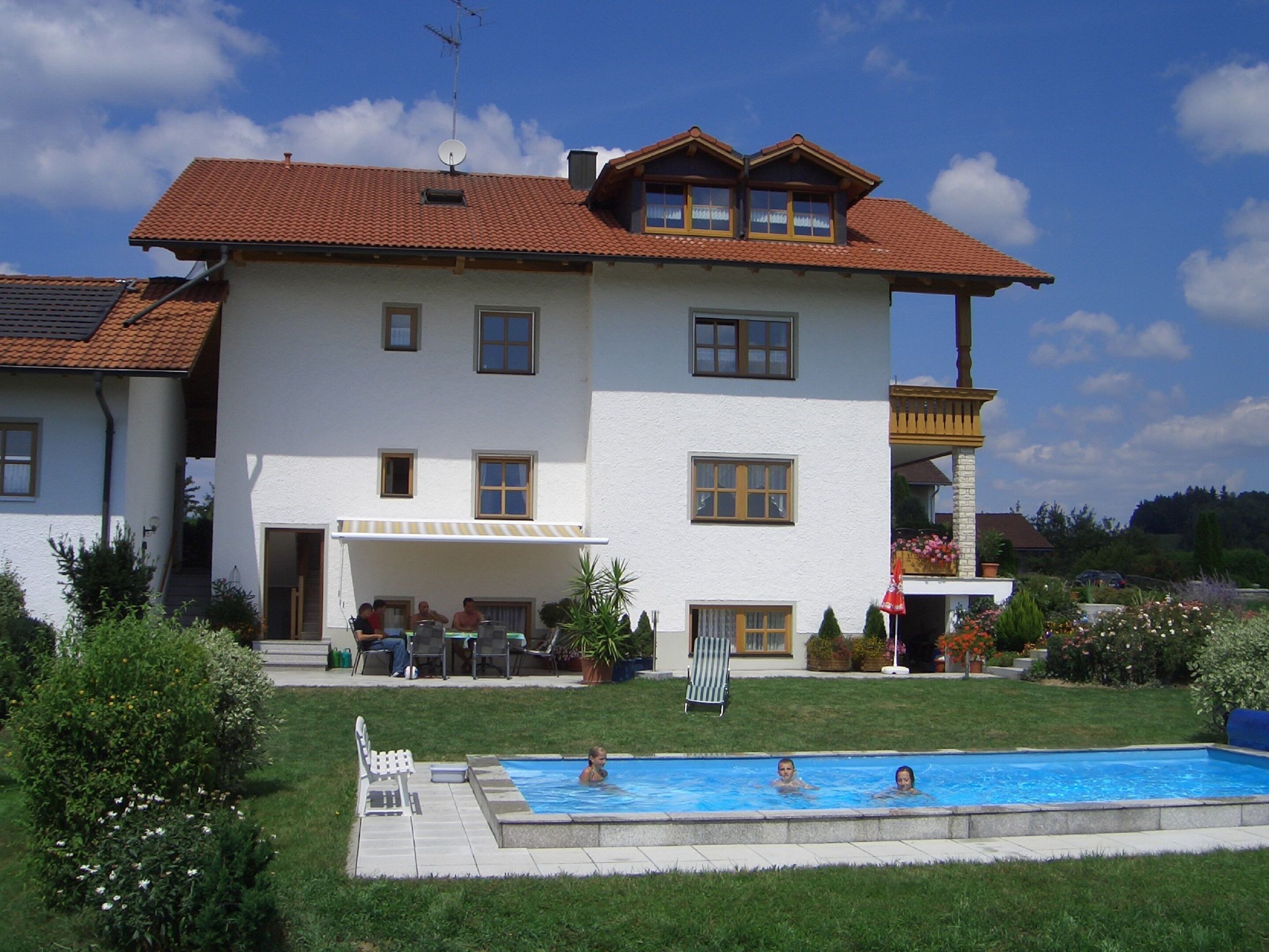 A two-story house with a swimming pool, a covered patio, and a garden.