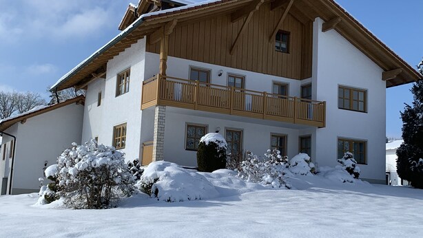 A large, two-story building with a wooden balcony and snow-covered surroundings. - Ferienwohnungen Martina (Windorf)