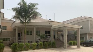 A two-story residential building with a covered porch, palm trees, and a car parked in front. - Haitel Guest Inn (Kano)
