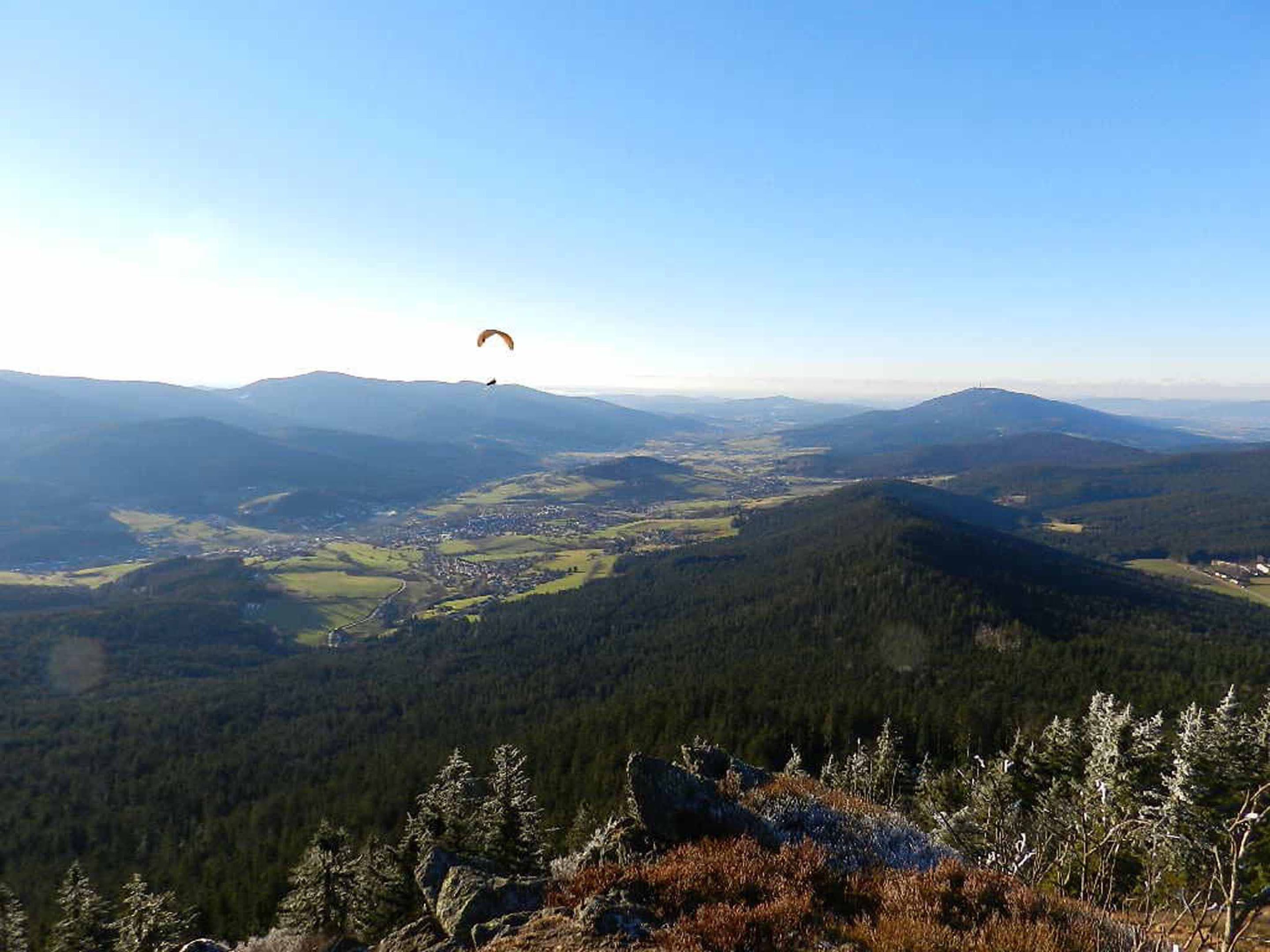 Paisaje montañoso con una persona parapentando a lo lejos.