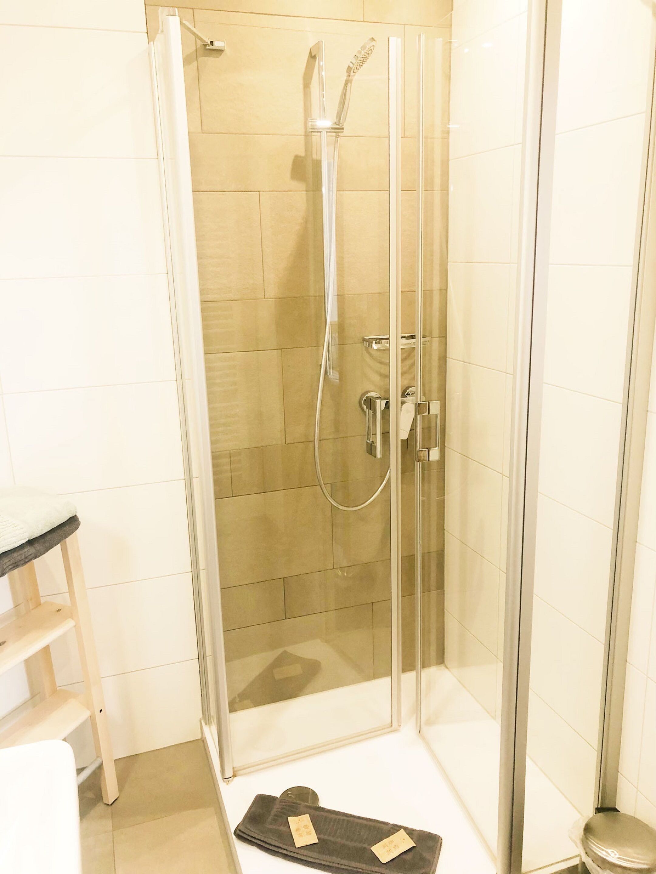 A glass-enclosed shower area with a handheld showerhead and a wall-mounted faucet.