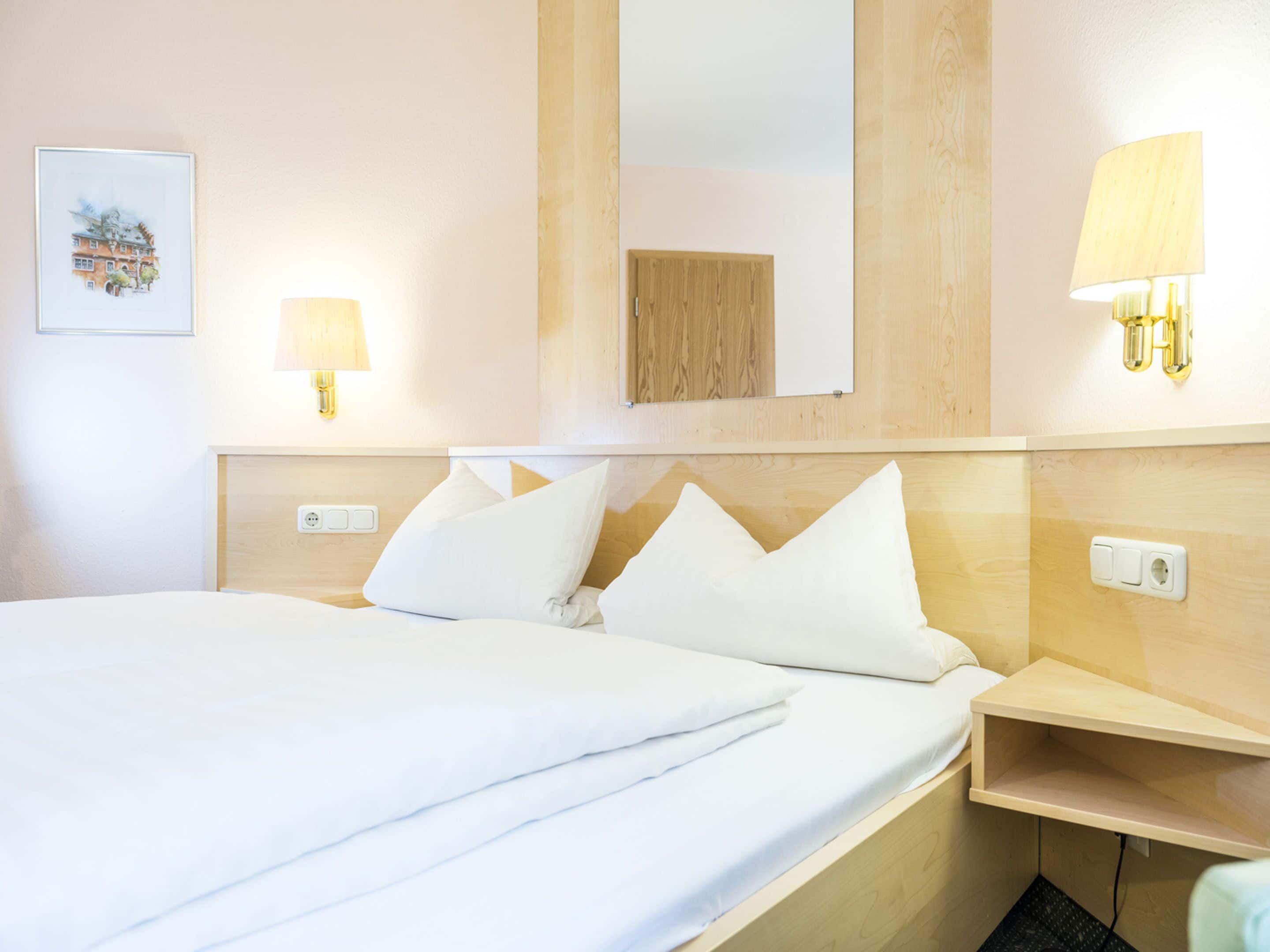 A hotel room with a large bed, two bedside lamps, a bedside table, a mirror, and a framed picture on the wall.