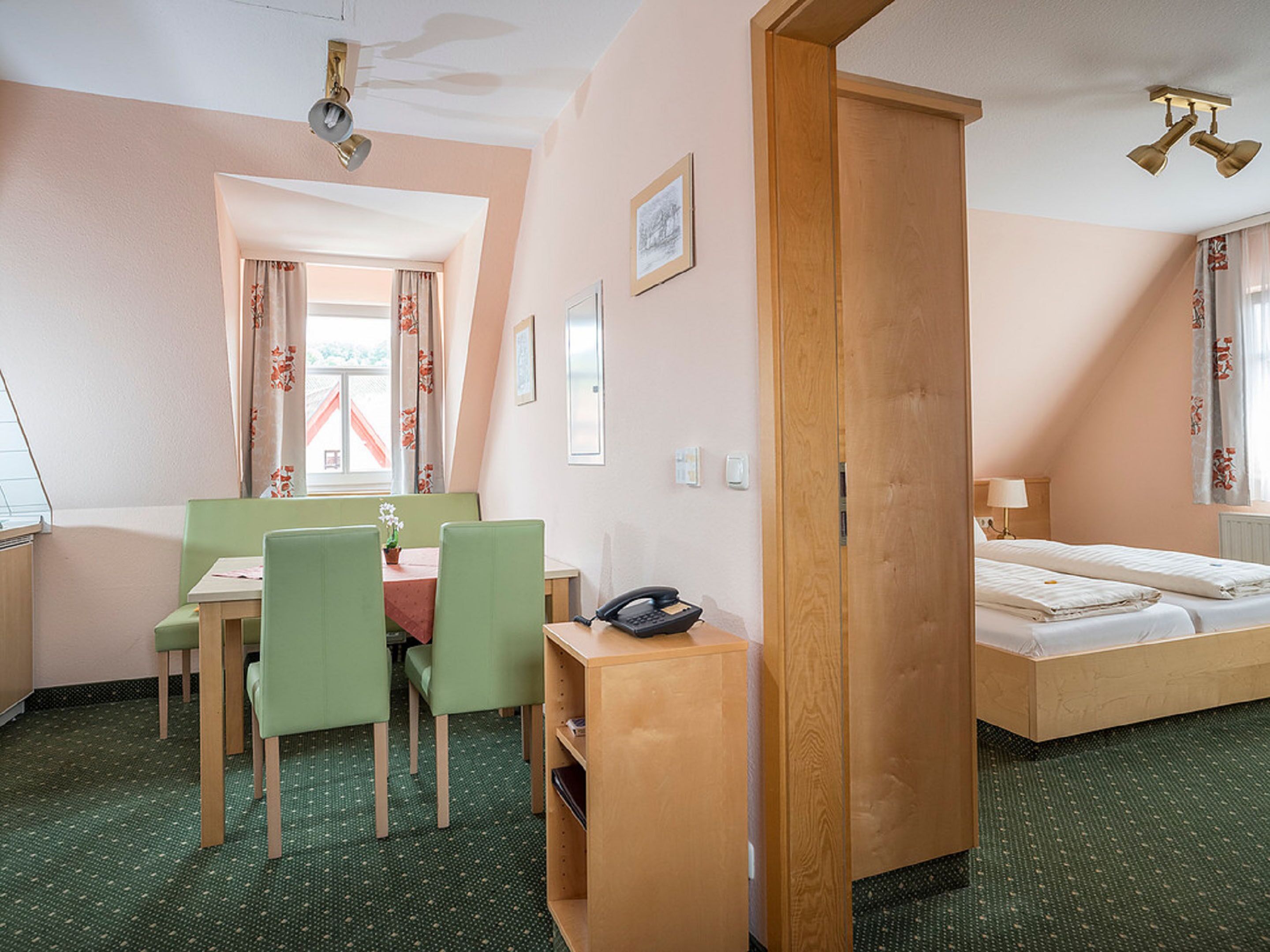 Habitación de hotel con cama, escritorio con teléfono, silla, mesita y ventana con cortinas.
