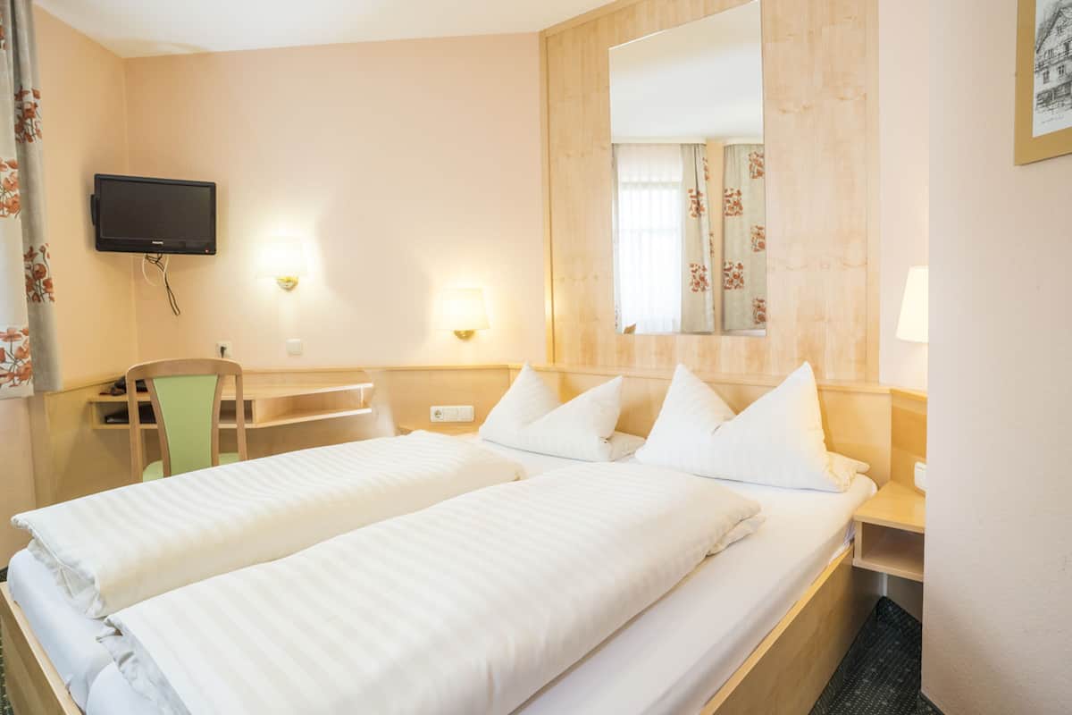 Een hotelkamer met twee bedden, een bureau, een stoel, een televisie en een grote spiegel.