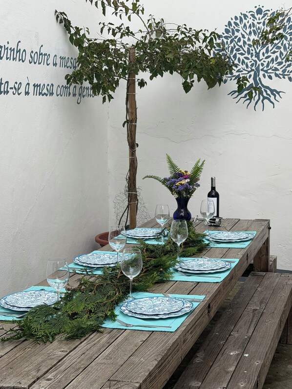 A wooden table set with blue and white plates, wine glasses, and a vase with flowers. - Large Home in city center of Ponta Delgada: yard, near marina (great for groups) (Ponta Delgada)