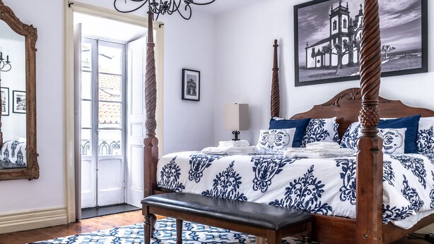 Um quarto com uma cama de dossel, um banco, um candelabro e um quadro na parede.