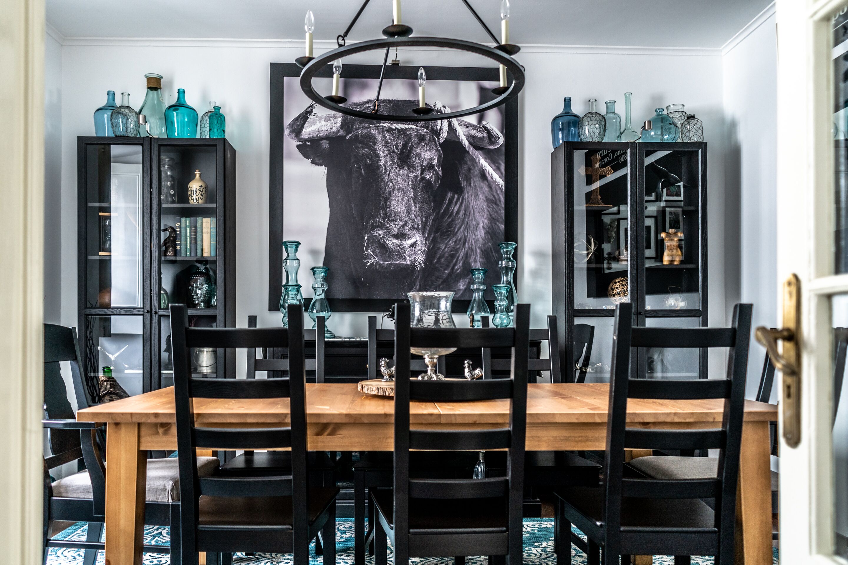 Un coin repas avec une table en bois et des chaises noires, entouré de meubles noirs aux portes vitrées, dans lesquels sont exposés divers objets.