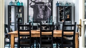 Uma sala de jantar com uma mesa de madeira e cadeiras pretas, cercada por armários pretos com portas de vidro que exibem diversos objetos.