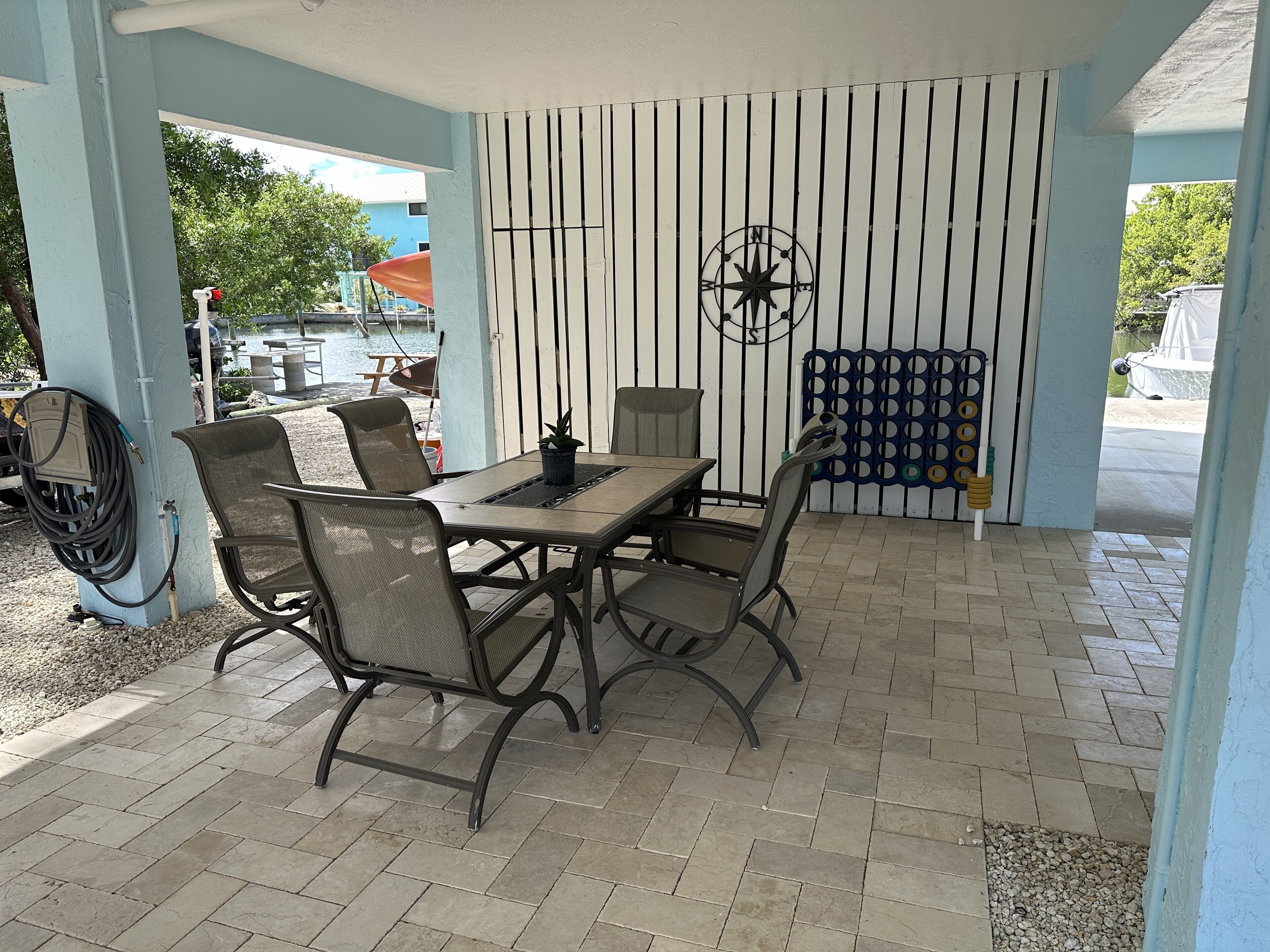 An outdoor patio with a table and chairs, a wall-mounted compass, and a blue fence with circular patterns.
