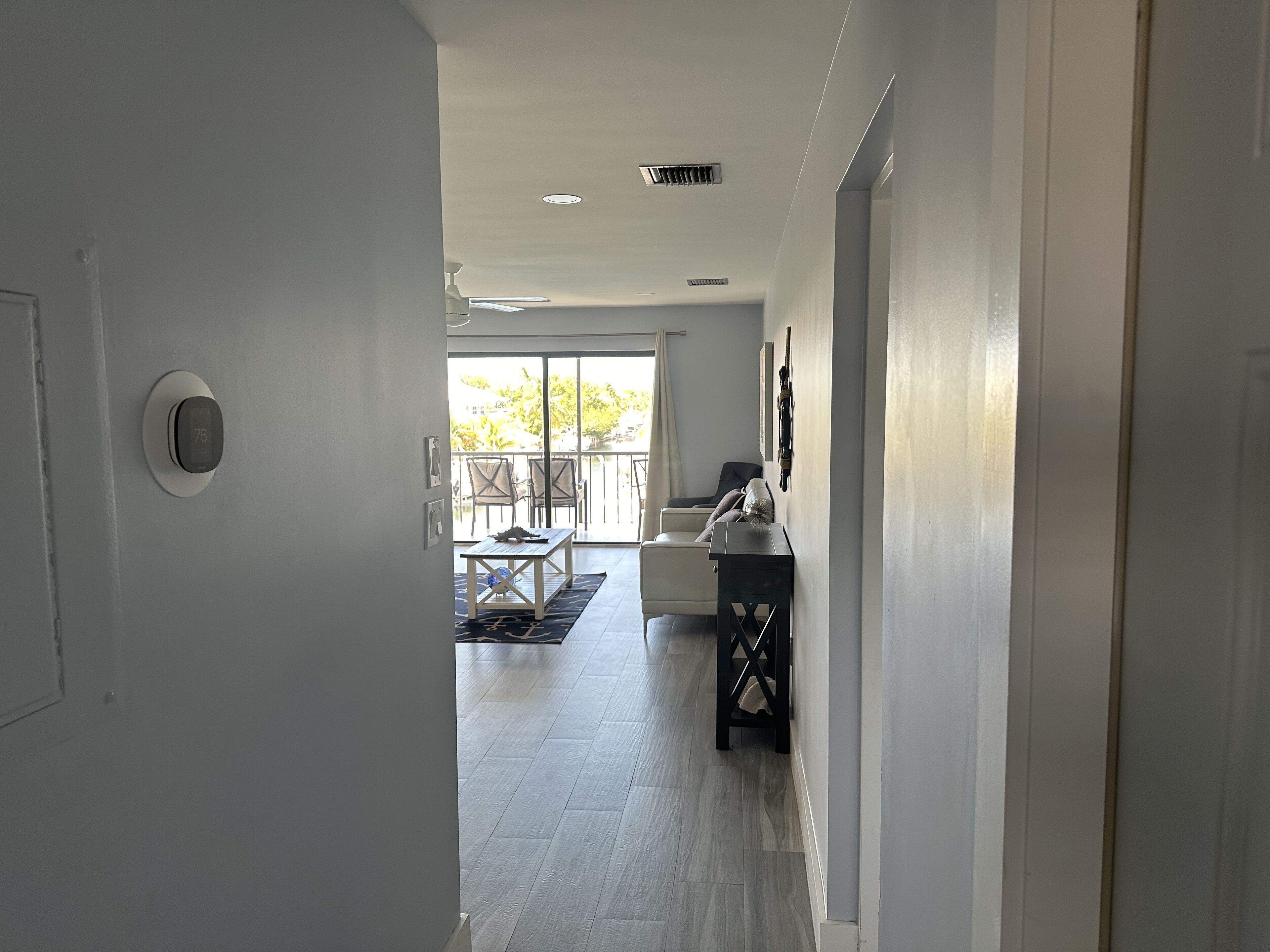 A hallway leading to a balcony with a dining area, a ceiling fan, and a thermostat.