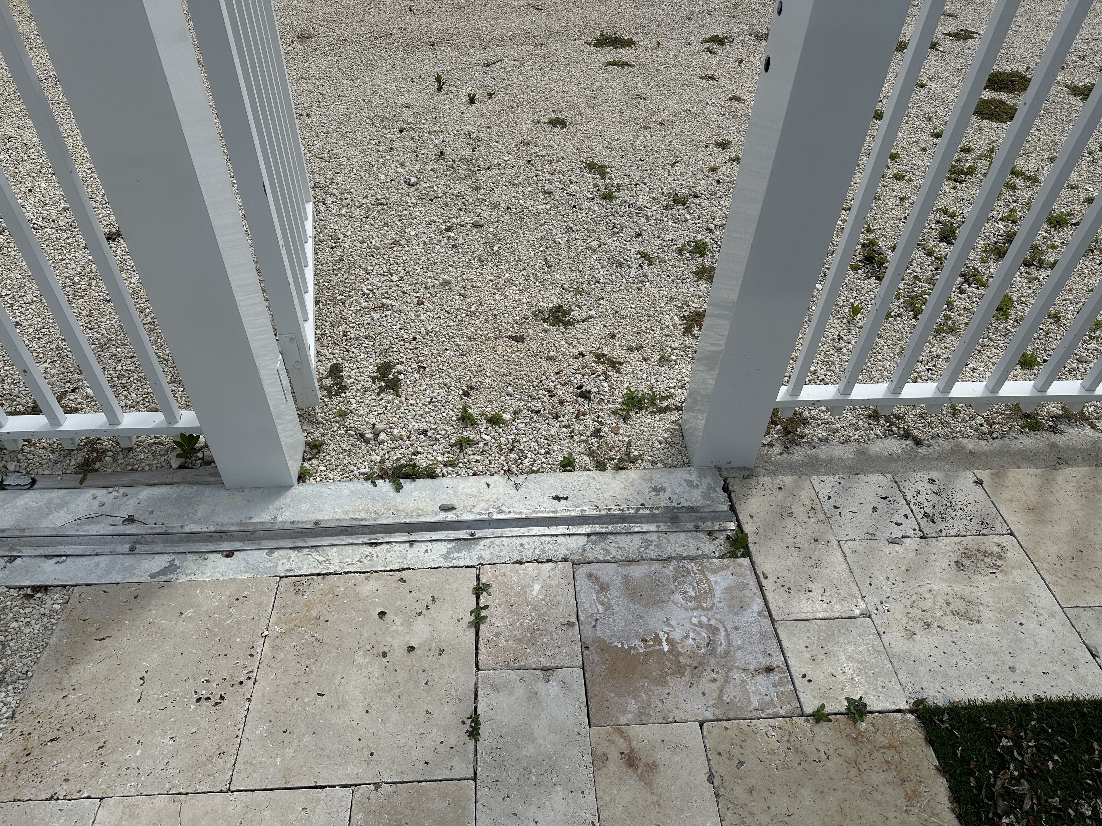 Un'area sterrata con una recinzione in metallo bianco e un vialetto in cemento.