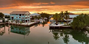 A waterfront property with a dock, reflecting buildings, and a sunset sky. - Re-energize at our spacious condo! Get 10% off stays of 7+ days. Book now! (Key Largo)