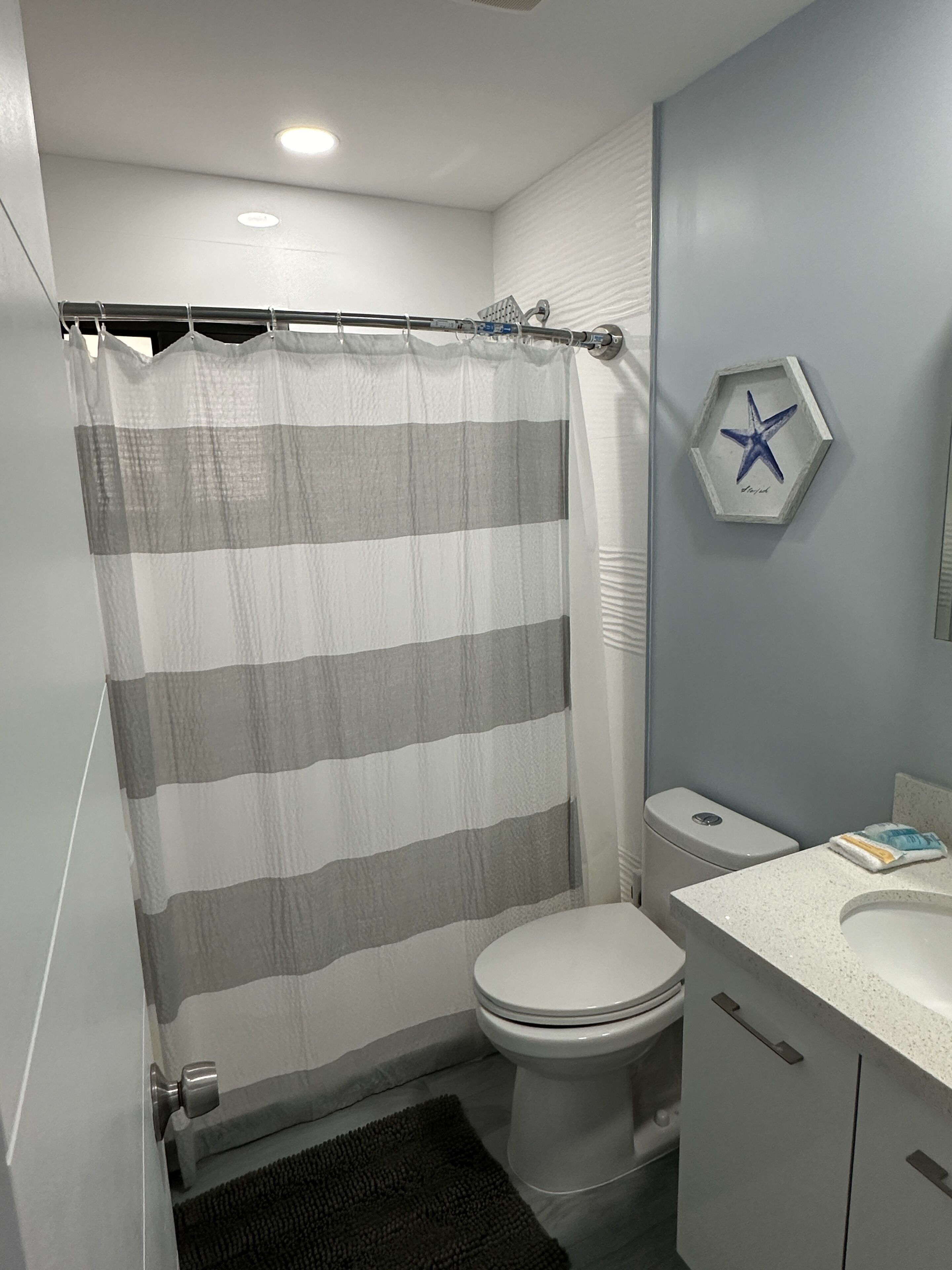 A bathroom with a shower curtain, toilet, sink, and a starfish decoration on the wall.