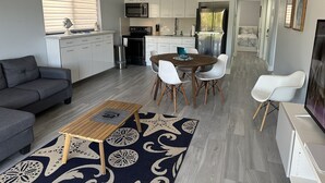 Een moderne keuken met witte kastjes, een magnetron en een koelkast. Er is een eethoek met een houten tafel en witte stoelen.