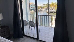 Een kamer met een grote schuifglazen deur die leidt naar een balkon met uitzicht op een jachthaven en gebouwen.
