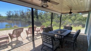 A covered patio with wicker furniture and a table, overlooking a lake.