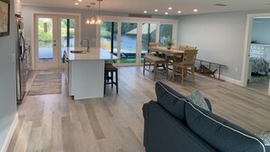 A modern kitchen with a central island, a dining area with wooden furniture, and a large sliding glass door leading to a view of a lake.