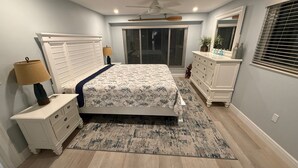 A bedroom with a bed, nightstands, a dresser, a ceiling fan, and a window with blinds.