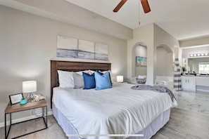 A modern bedroom with a large bed, bedside tables, a ceiling fan, and a view into the bathroom.