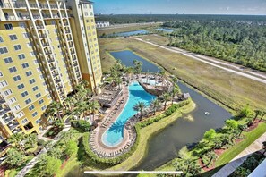 A high-rise hotel with a central swimming pool, surrounded by lush greenery and a small lake.