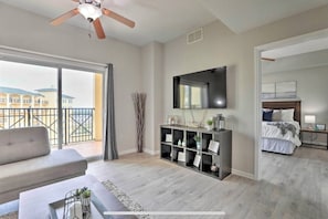 A modern living room with a sofa, a TV mounted on the wall, and a balcony with a view of buildings.
