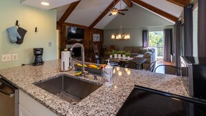 A kitchen with granite countertops, a sink, a stove, and a ceiling fan. There is a dining area with a table and chairs, and a television mounted on the wall.