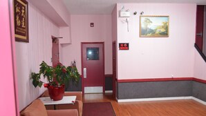 Quarto com porta vermelha, um quadro, placa de 'Proibido Fumar', uma planta e rodapé vermelho e branco.