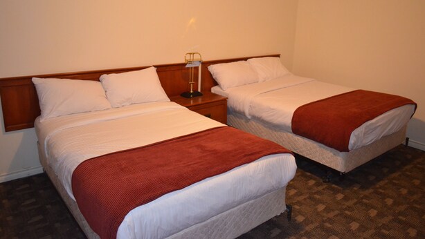 Duas camas de solteiro com cabeceiras de madeira, roupa de cama branca e um cobertor vermelho em cada uma.