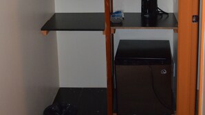 Quarto de canto com geladeira preta, cafeteira e lixeira.