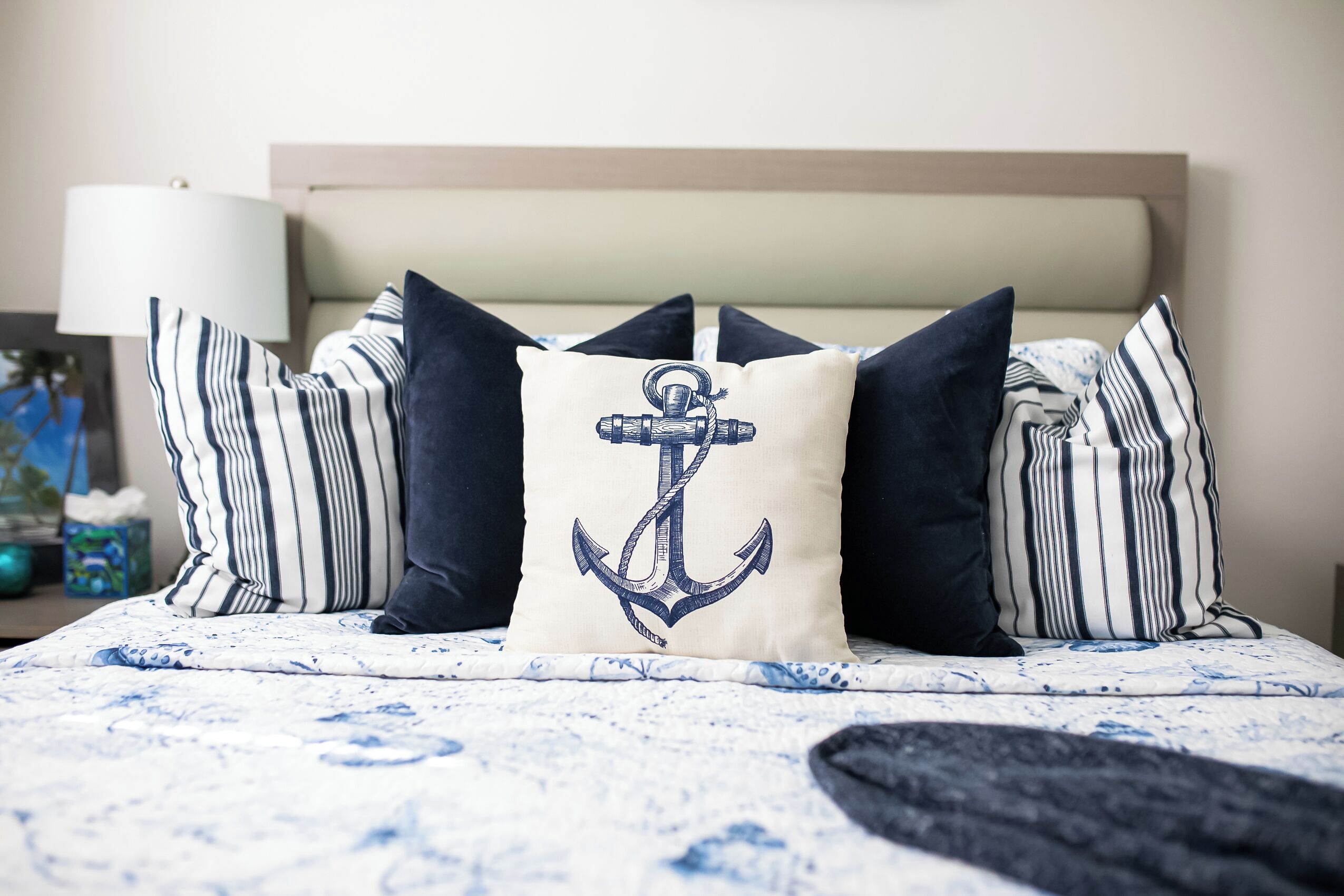 Una cama con ropa de cama a rayas y un cojín con diseño de ancla.