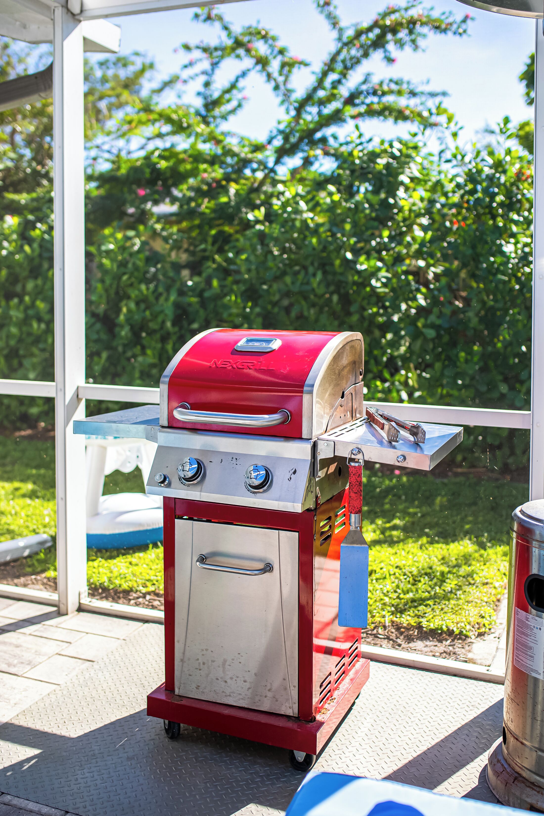 A red and white portable grill with a digital display, placed on a covered patio with a view of greenery.
