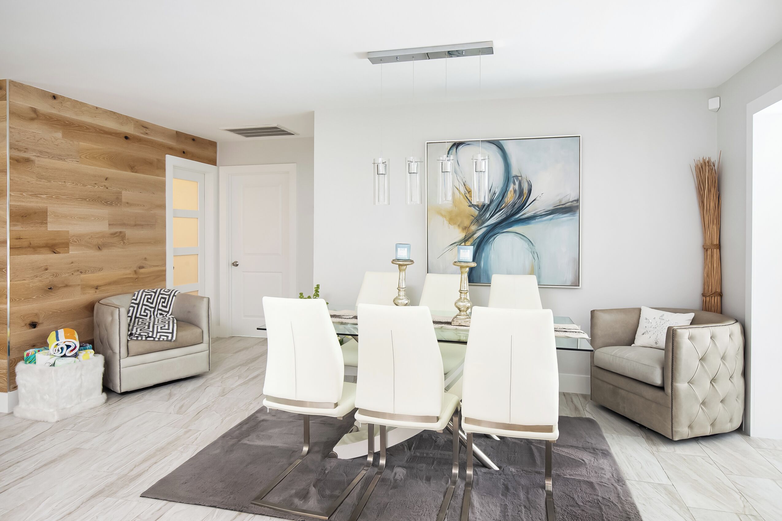 A modern living room with a dining area, featuring a wooden accent wall, a large abstract painting, and a glass dining table with white chairs.