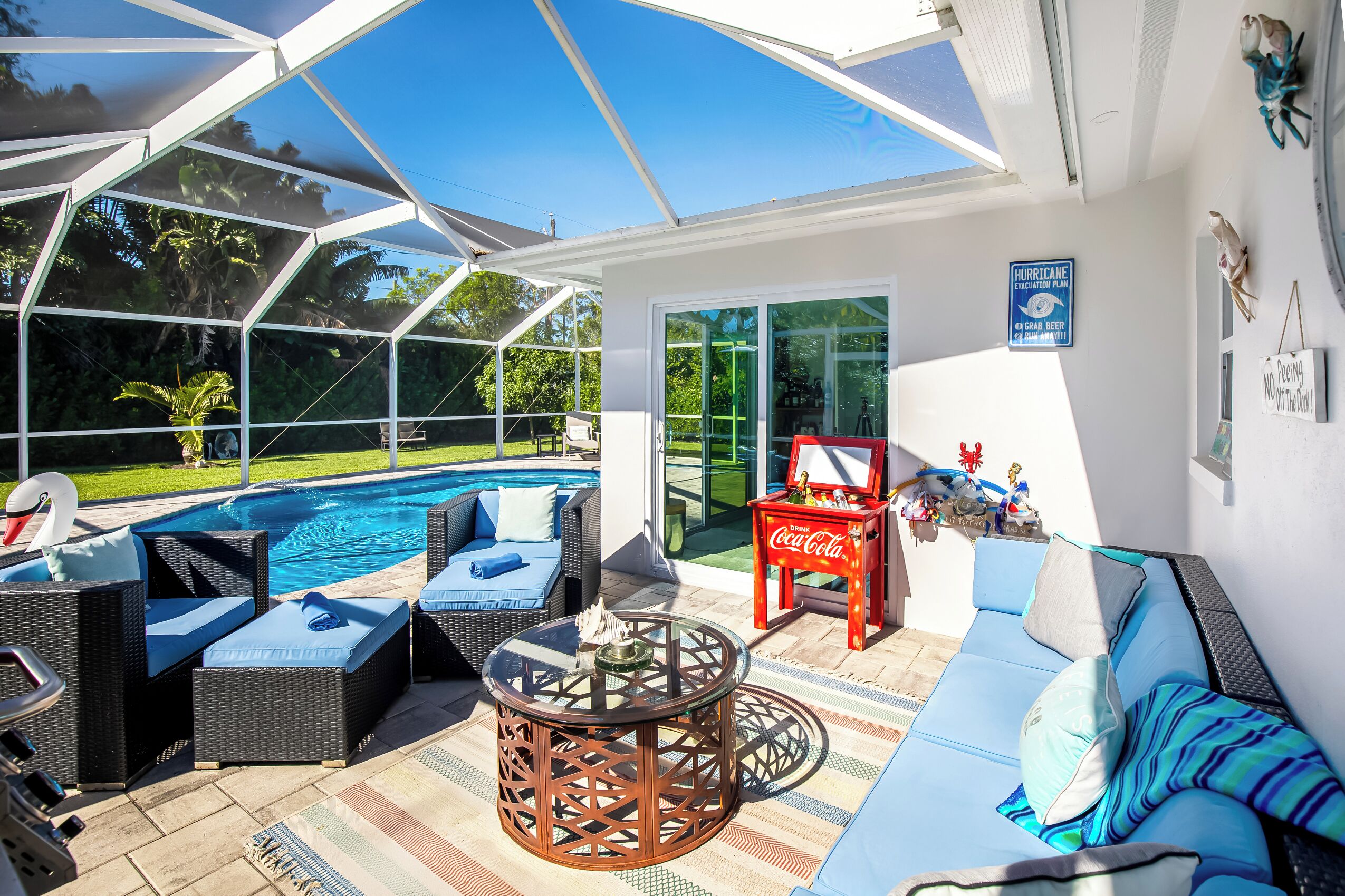 A sunlit outdoor patio with a pool, wicker furniture, and a Coca-Cola branded table.