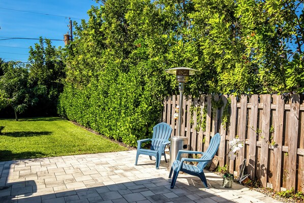 Relax in the serene patio area with a brick floor, surrounded by lush greenery and a wooden fence.